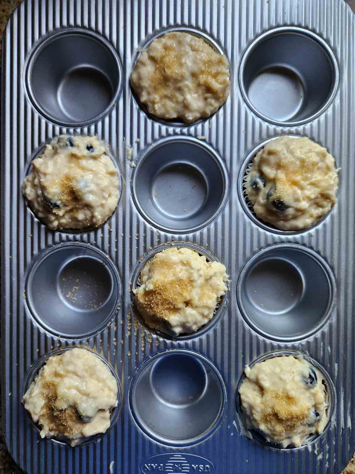 Muffin batter in a muffin tin filled every other well.