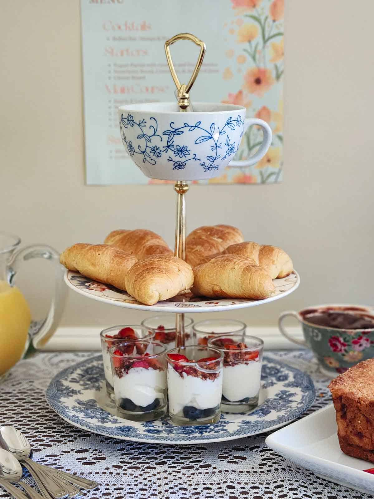 Charming tea display featuring croissants, layered desserts, and a floral teacup.