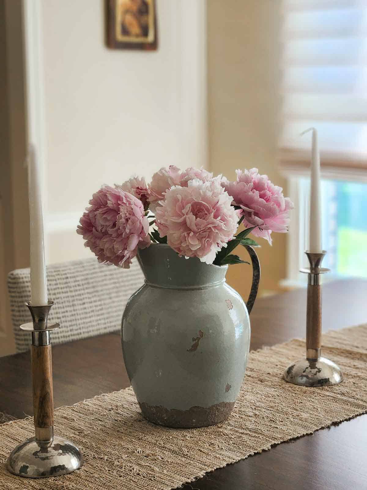 A blue antique pitcher with pink peonies on a wooden table.