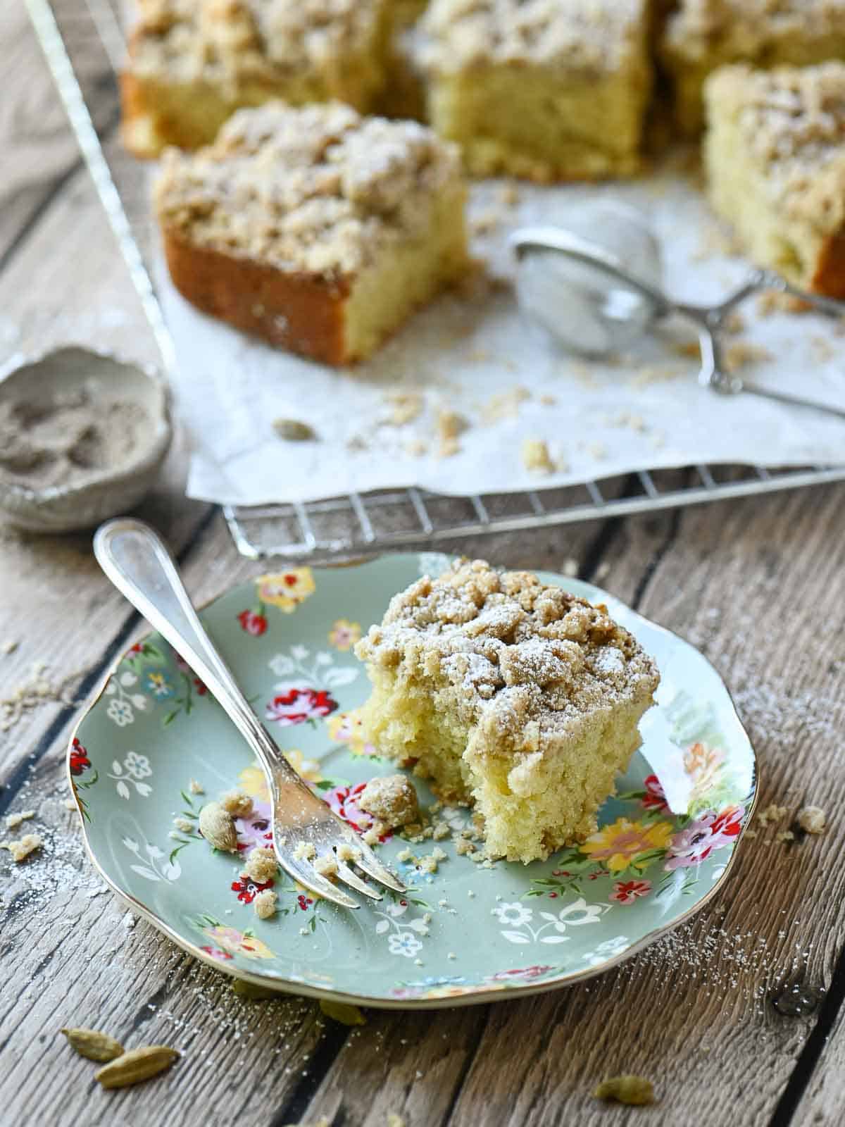 A slice of coffee cake on a floured plate with a fork to the left.