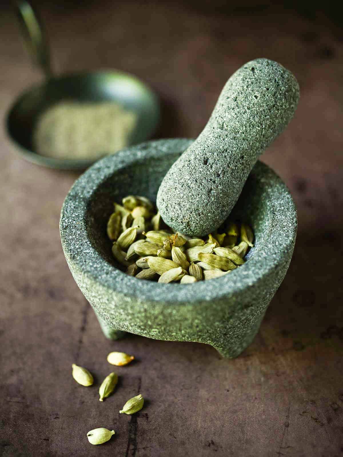 Cardamom pods in a mortar with a pestle.