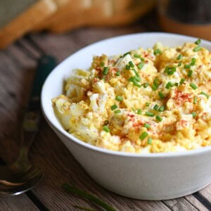 Egg salad in a white bowl with paprika and chives placed on a wooden table.