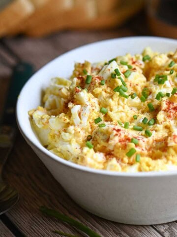 Egg salad in a white bowl with paprika and chives placed on a wooden table.