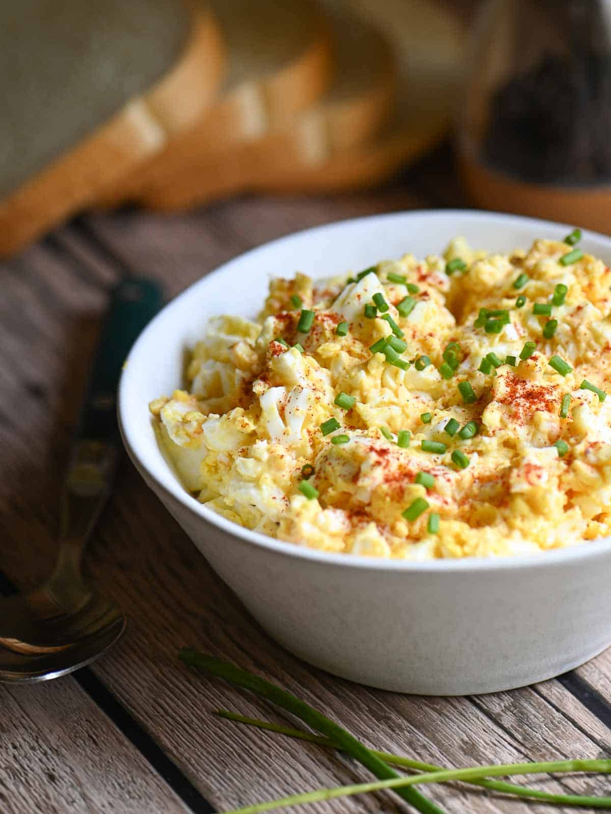 Egg salad in a white bowl with paprika and chives placed on a wooden table.