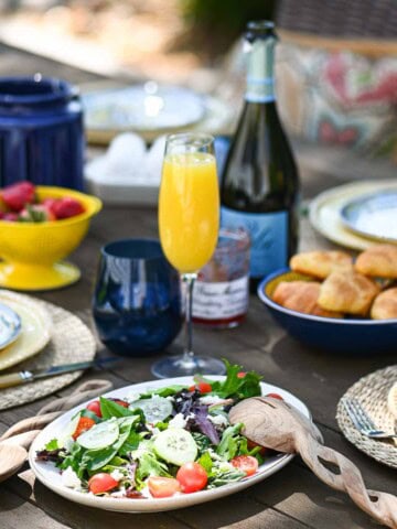 Casual outdoor brunch served on a wooden table with food and beverages in the background.