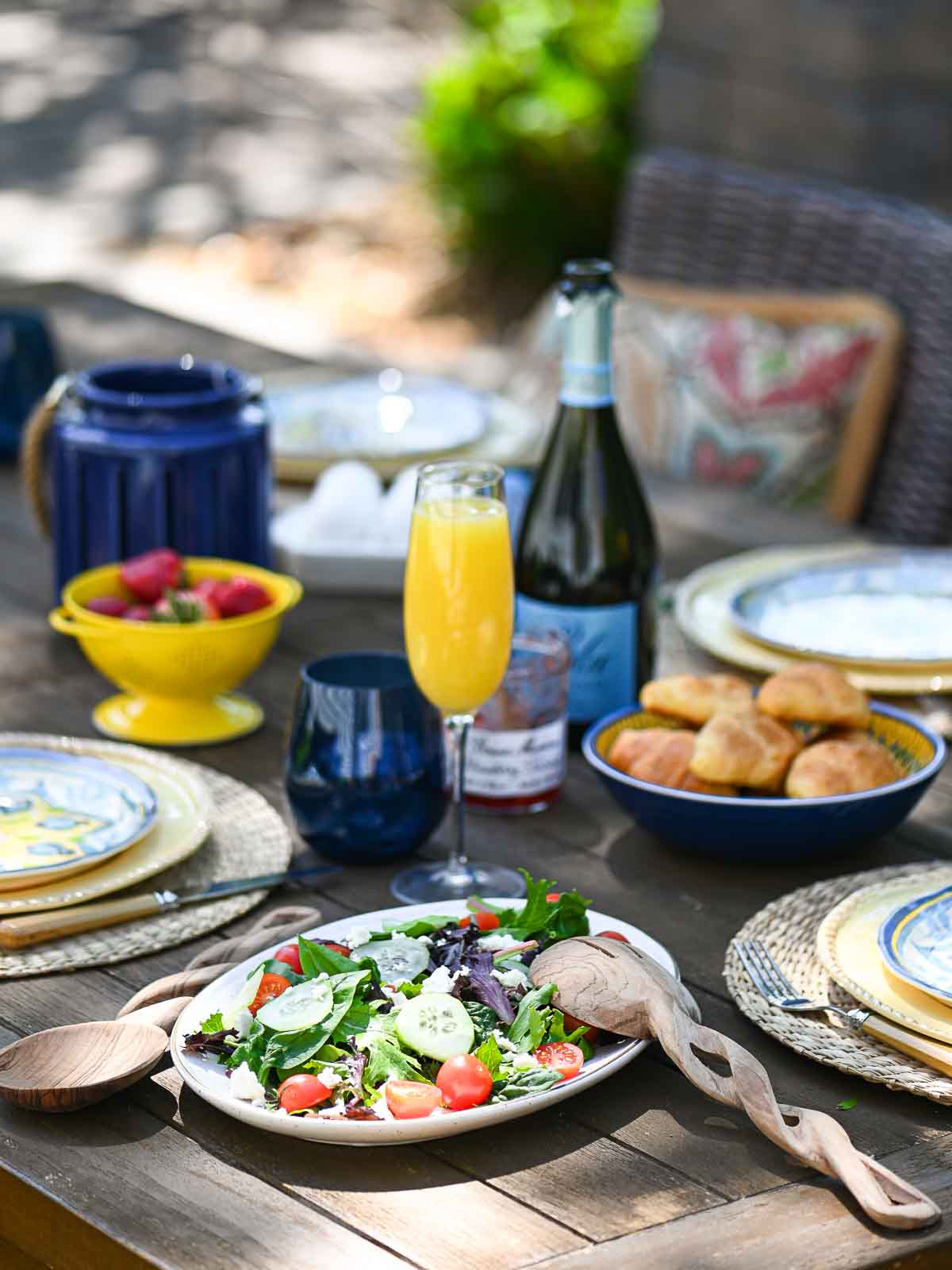 Casual outdoor brunch served on a wooden table with food and beverages in the background.