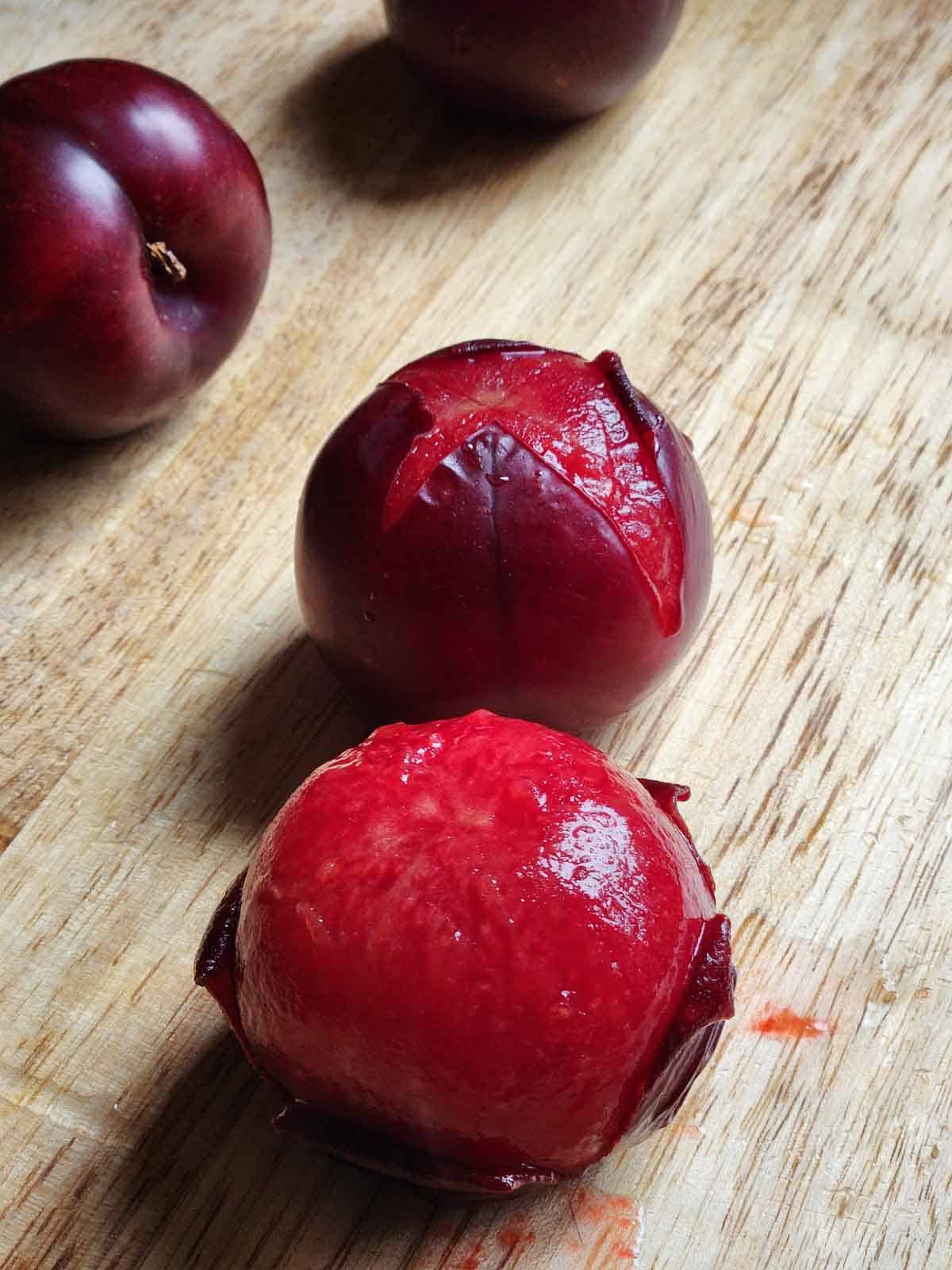 Peeled plums showing the red flesh on a wooden board.