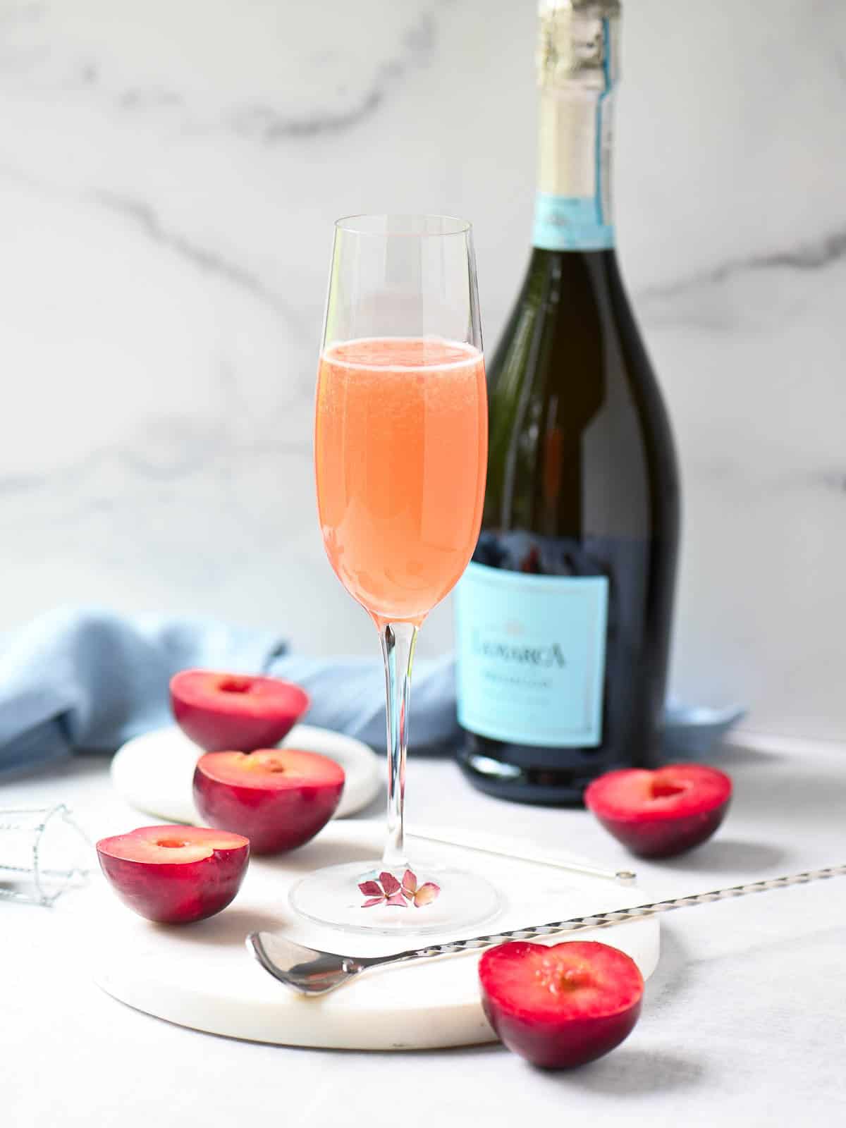 A Bellini in a stemmed flute with Prosecco in the background.