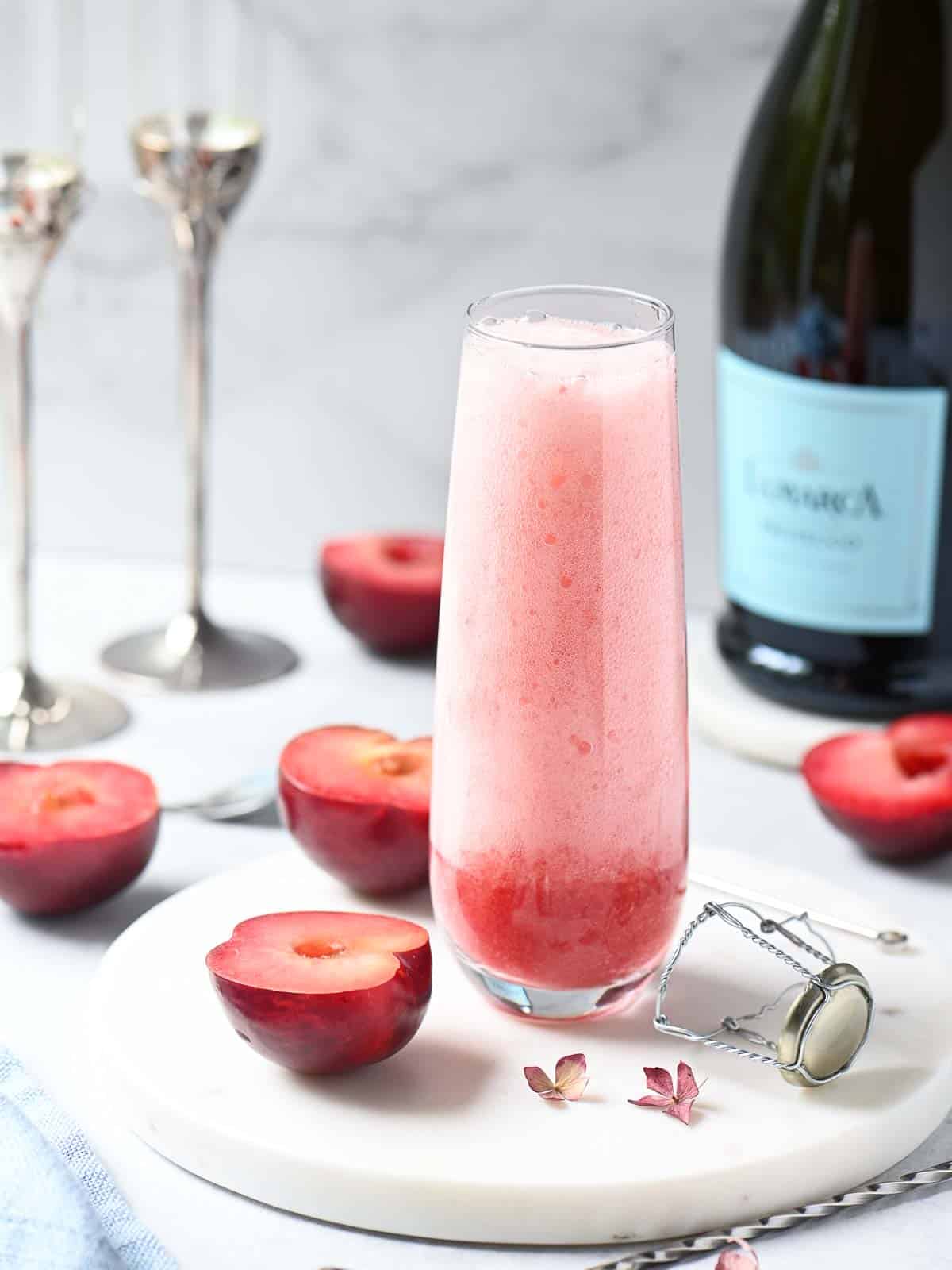 A plum Bellini in a clear Champagne flute with fresh plums around it.