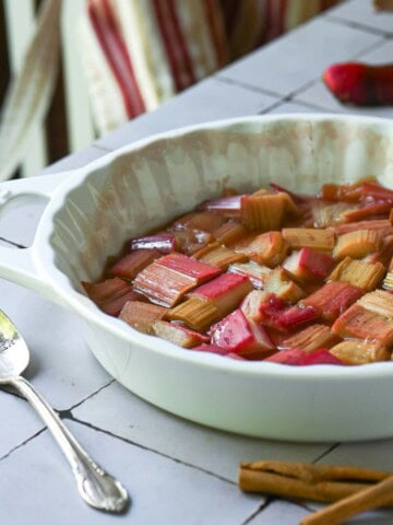 Roasted rhubarb in a white baking dish with a striped apron in the back.
