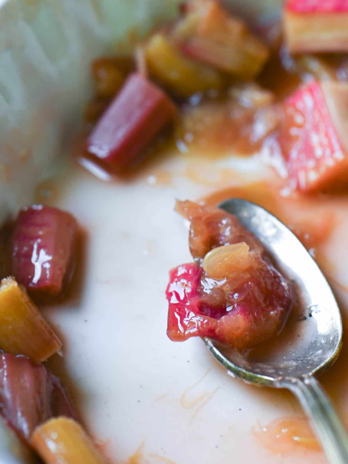 Close-up of rhubarb compote in a white baking dish with a spoon.