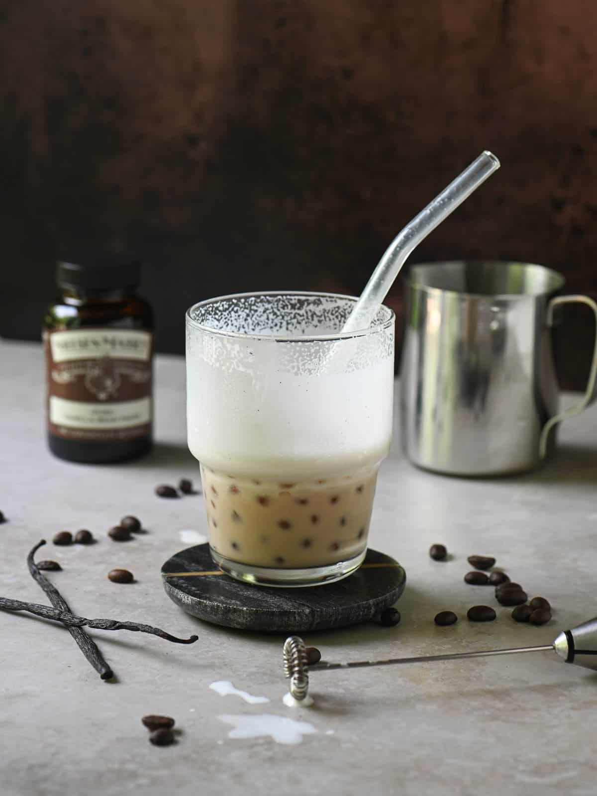 Eye-level view of a half-empty coffee latte in a clear cup on a beige surface.