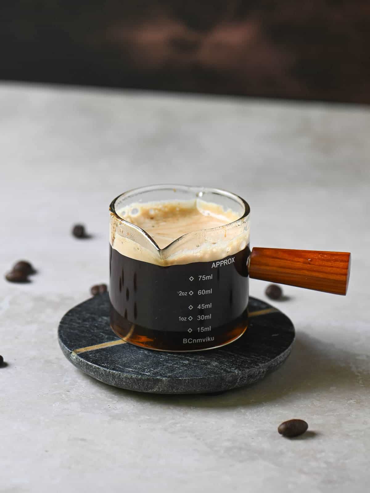 Espresso into a small clear glass holder with a wooden handle.