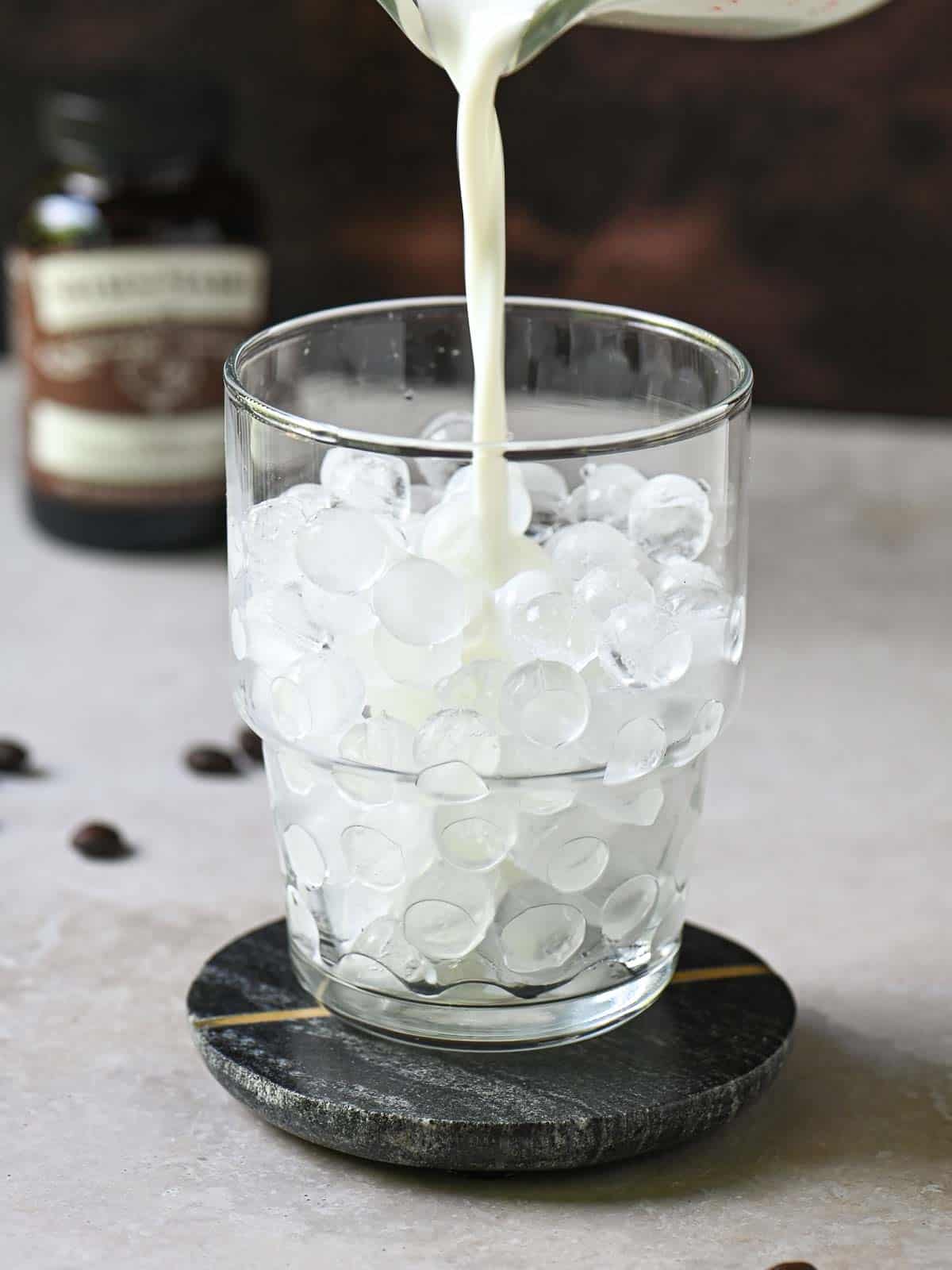 Milk being poured into a clear glass with ice.