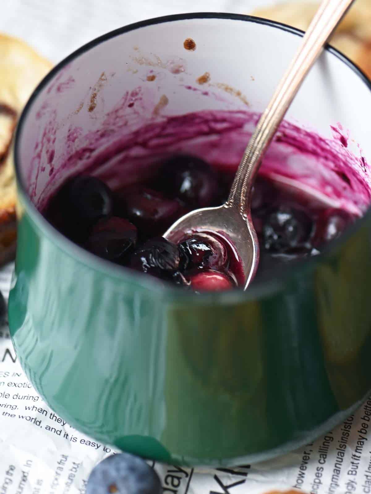 Warmed blueberry sauce in a small green saucepan.