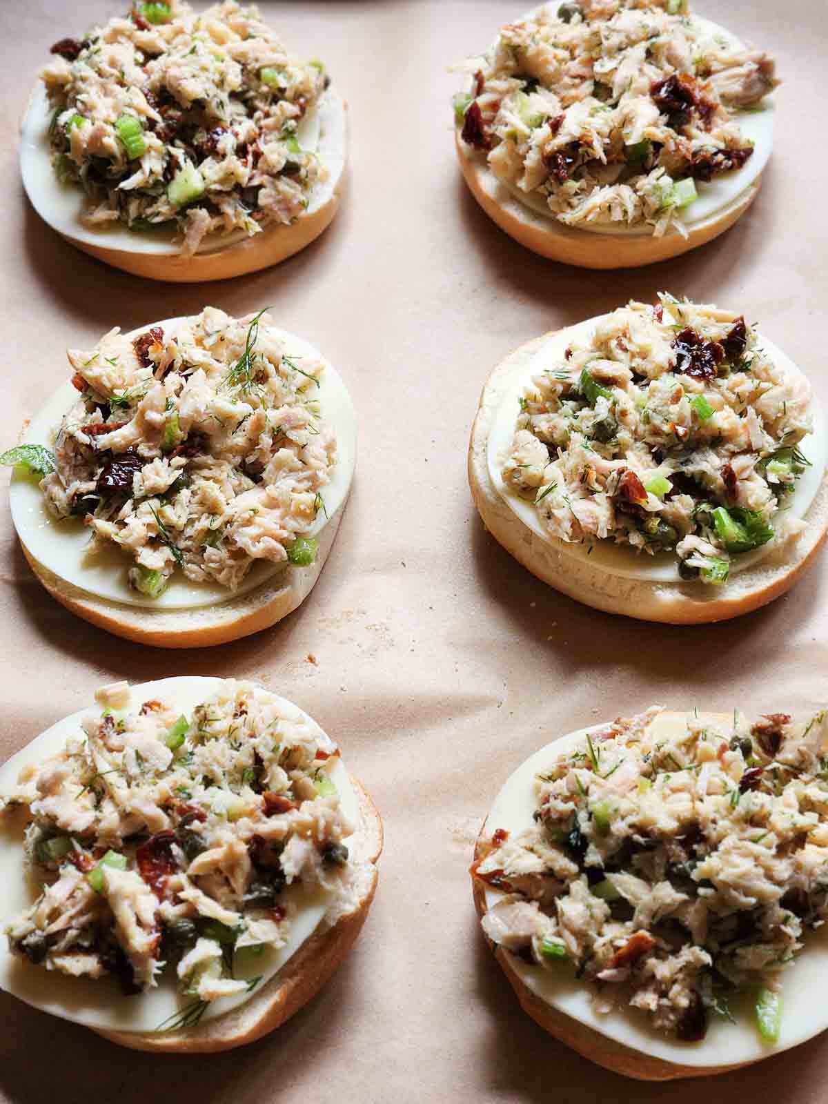 Six tuna bagels on a baking sheet with brown parchment paper.
