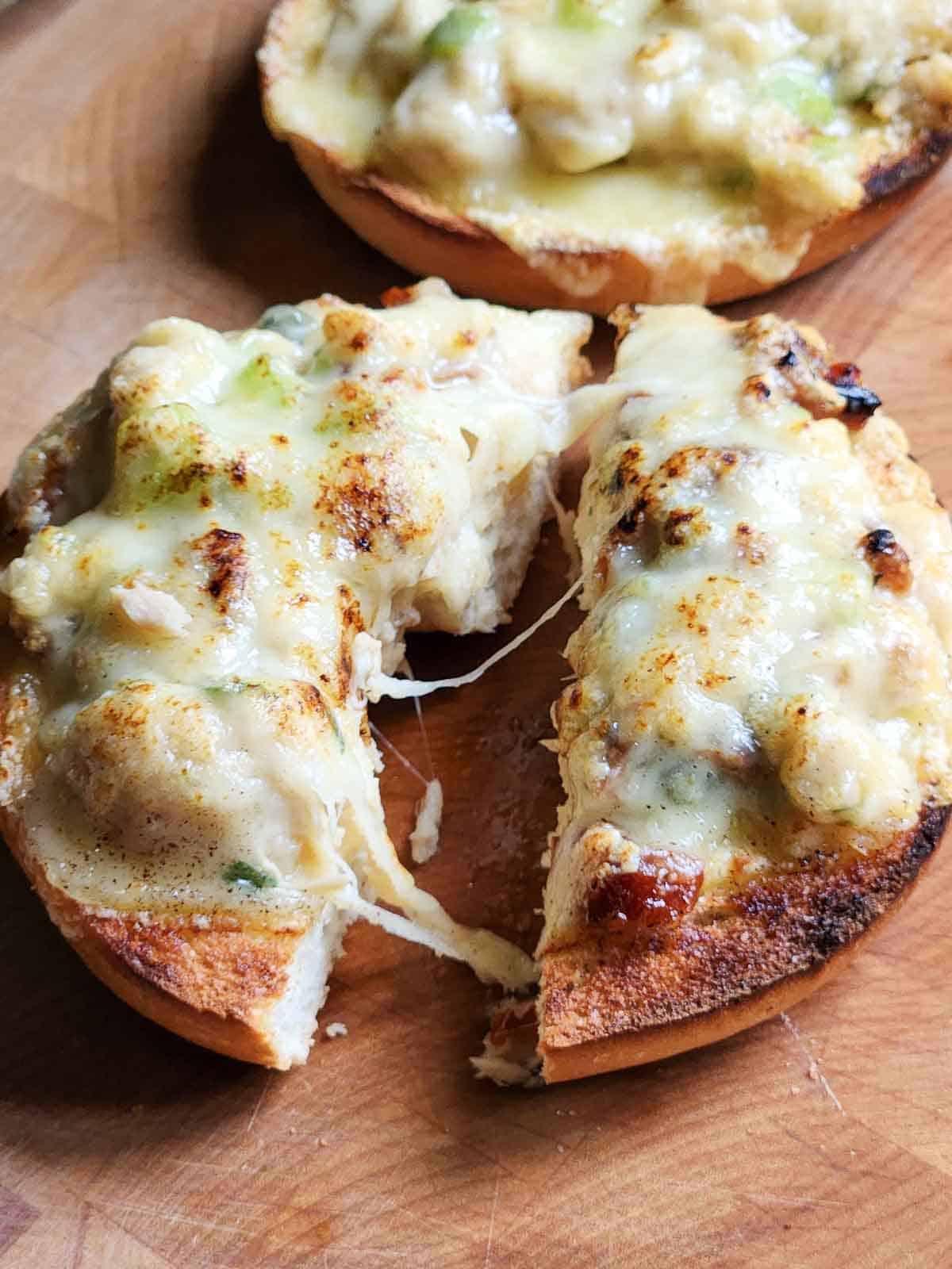 A tuna melt bagel cut in half with cheese pulled.