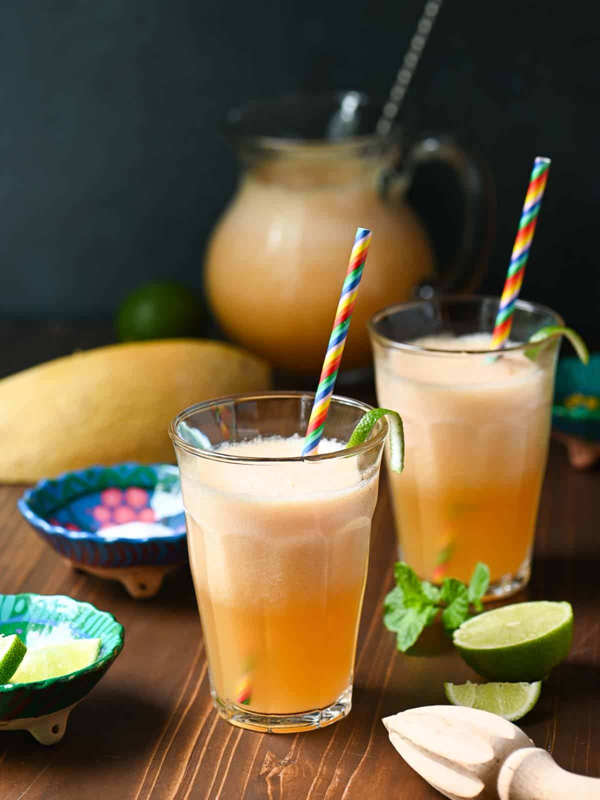 Two clear glasses of cantaloupe drink with straws on a wooden board with limes.