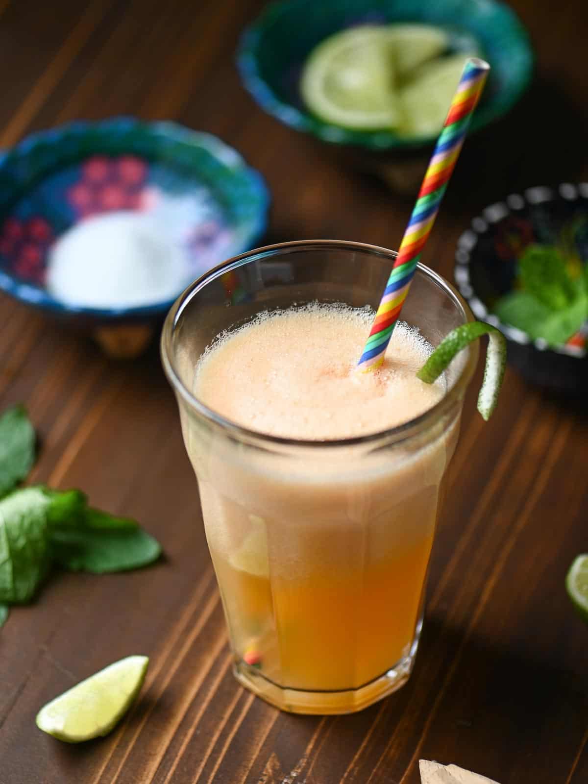 Close up of a clear glass of cantaloupe juice with bright green containers in the background.