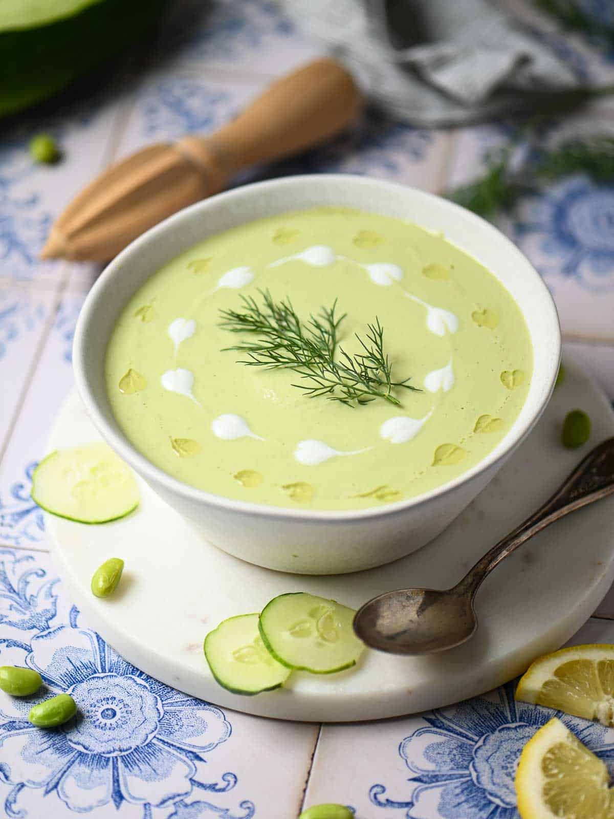 Overhead of cucumber soup in a white bowl with swirls of yogurt and oil.