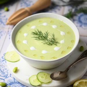 Overhead of cucumber soup in a white bowl with swirls of yogurt and oil.