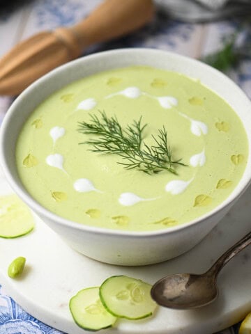 Overhead of cucumber soup in a white bowl with swirls of yogurt and oil.