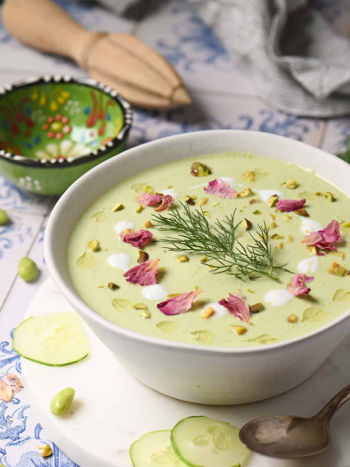 Cucumber soup in white bowls with various toppings on a blue marble top.