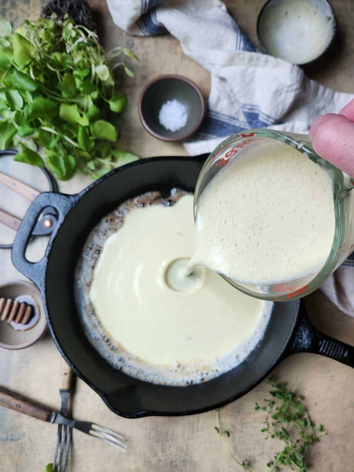 Batter being poured into a hot black skillet.