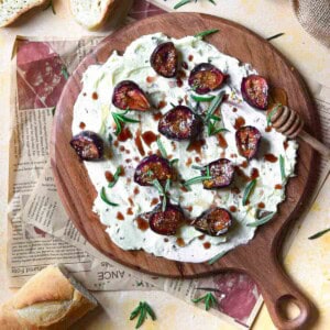 Overhead of figs, rosemary and butter on a round wooden board.