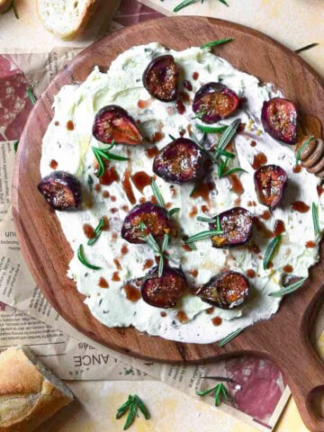 Overhead of figs, rosemary and butter on a round wooden board.