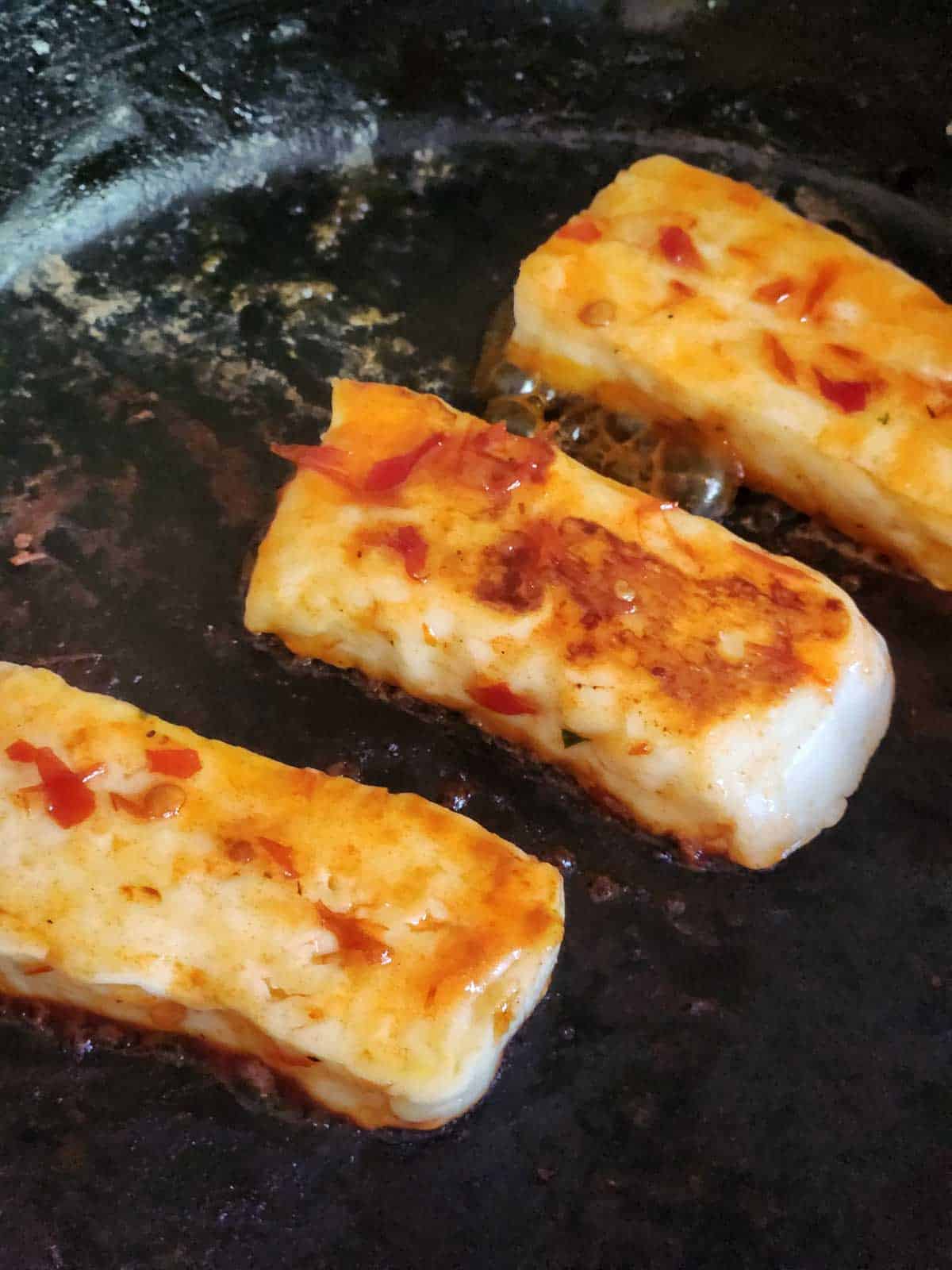Three pieces of fried halloumi in a black skillet.