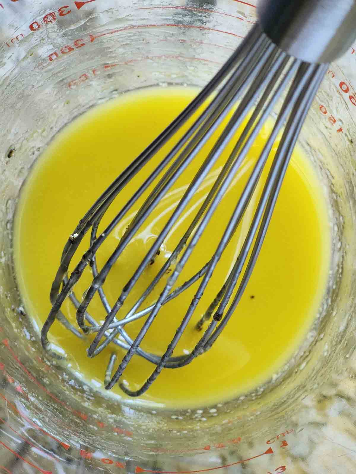 Overhead of a lemon dressing in a clear cup with a whisk.