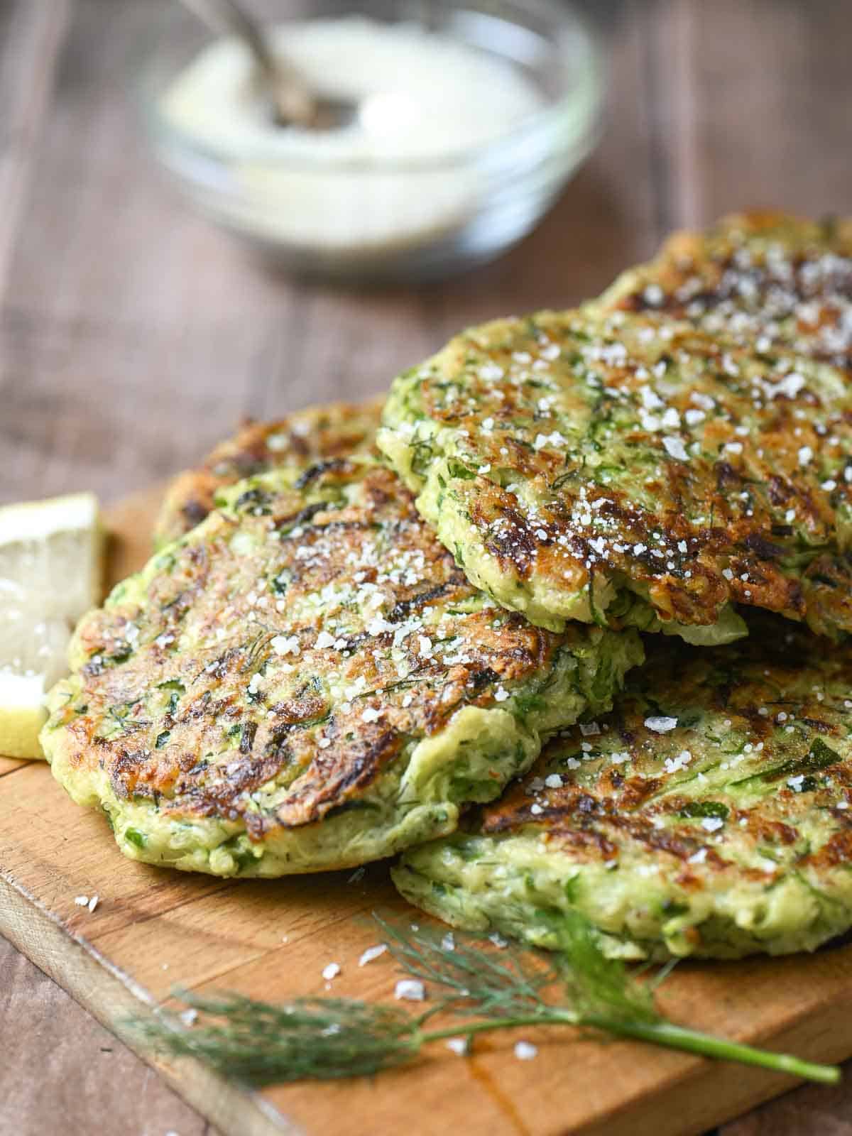 Zucchini pancakes on a wooden board with lemon and dill.