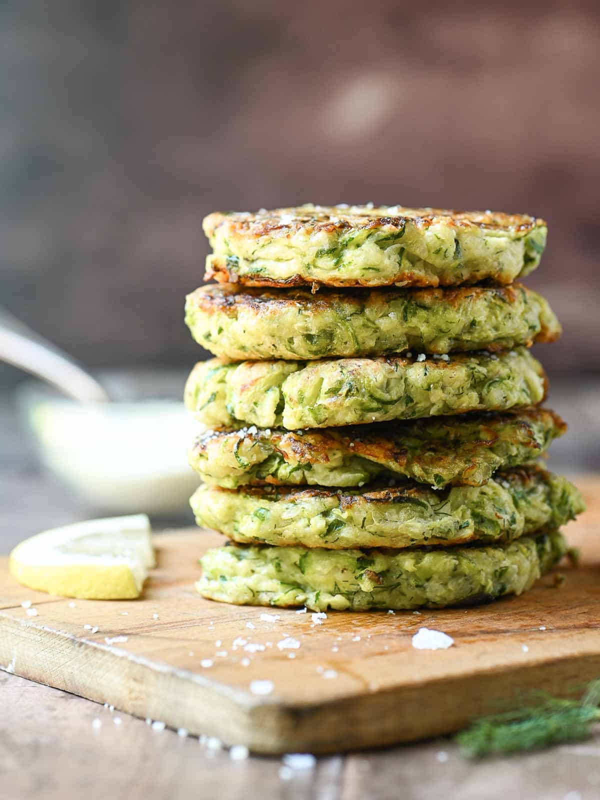 Parmesan zucchini pancakes stacked high on a wooden board.