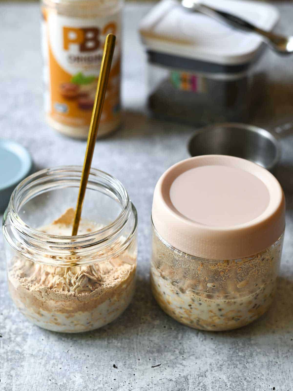 Two jars of overnight oats being prepared on a concrete surface.