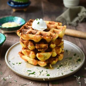 A stack of savory waffles on brown plate with small bowls in the back.