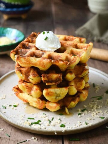 A stack of savory waffles on brown plate with small bowls in the back.