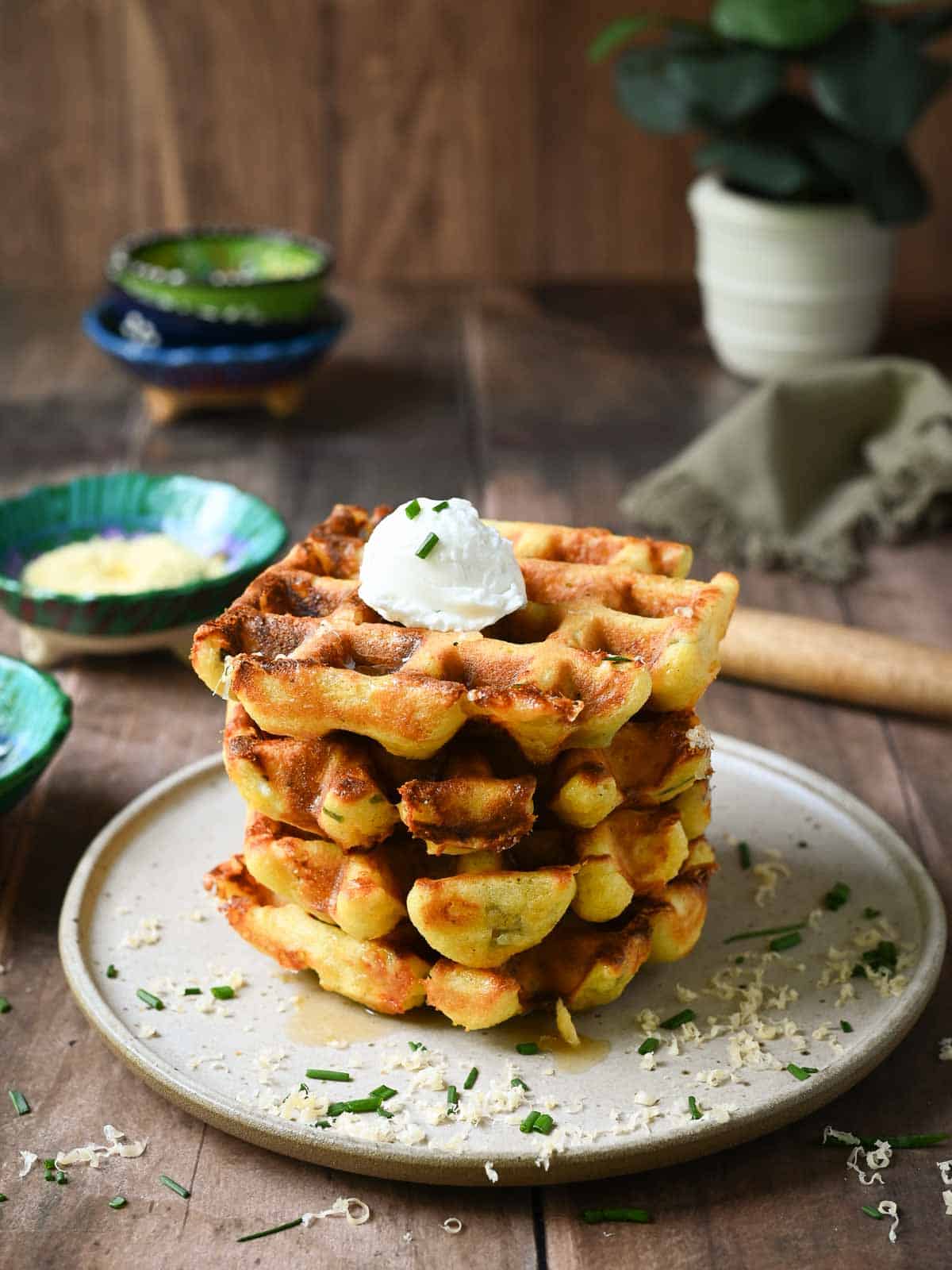 A stack of savory waffles on brown plate with small bowls in the back.