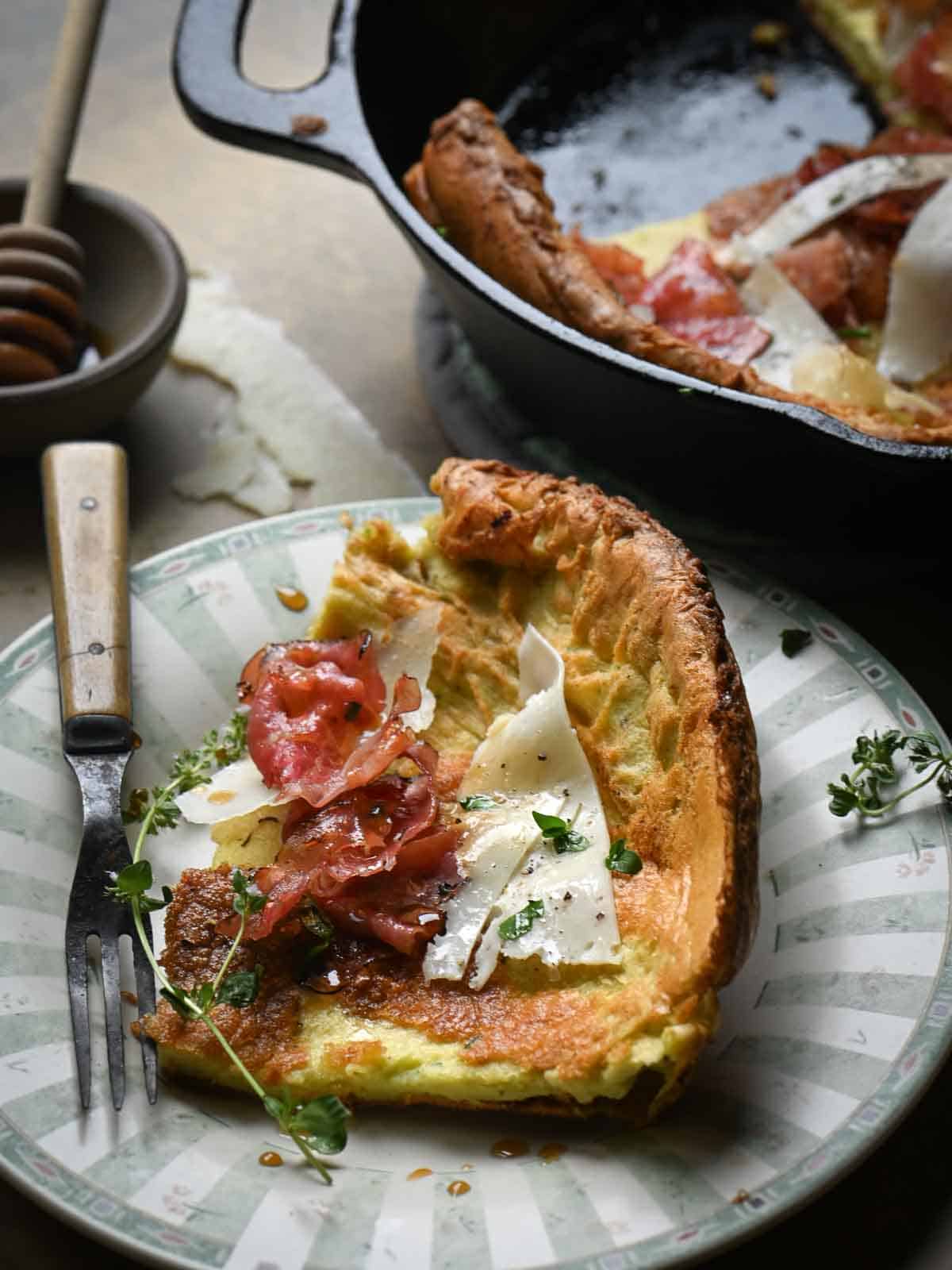 A slice of Dutch baby pancake on a small plate with a fork to the left.