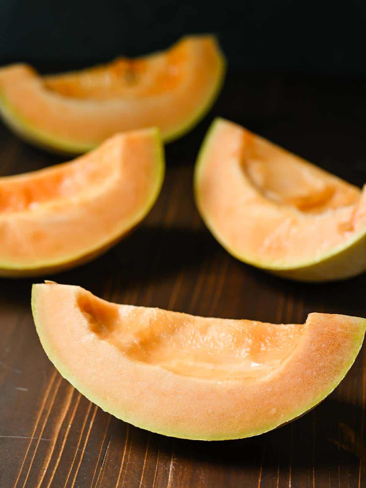 Sliced quarters of cantaloupe on a wooden board.