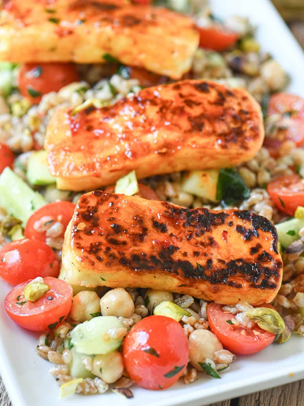 Close-ip of grilled haloumi over a salad on a white plate.