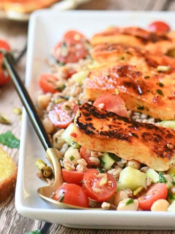 Eye level view of grilled halloumi on a farro salad in a white plate.