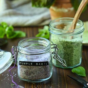 Two clear jars of purple and green basil salt.