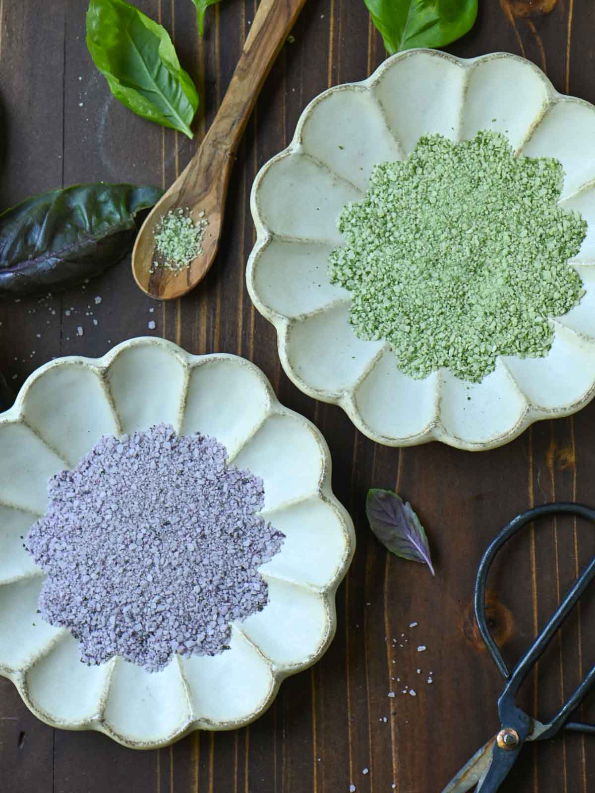Overhead view of purple and green basil salt in beige plates on a wooden surface.