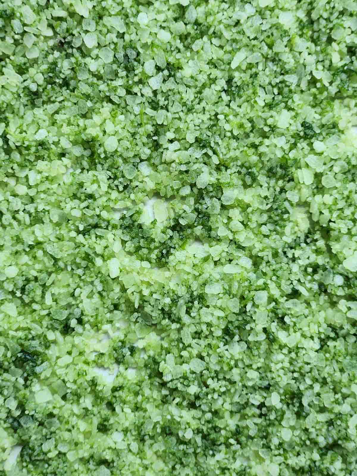 Overhead of green basil salt spread out on a baking sheet.