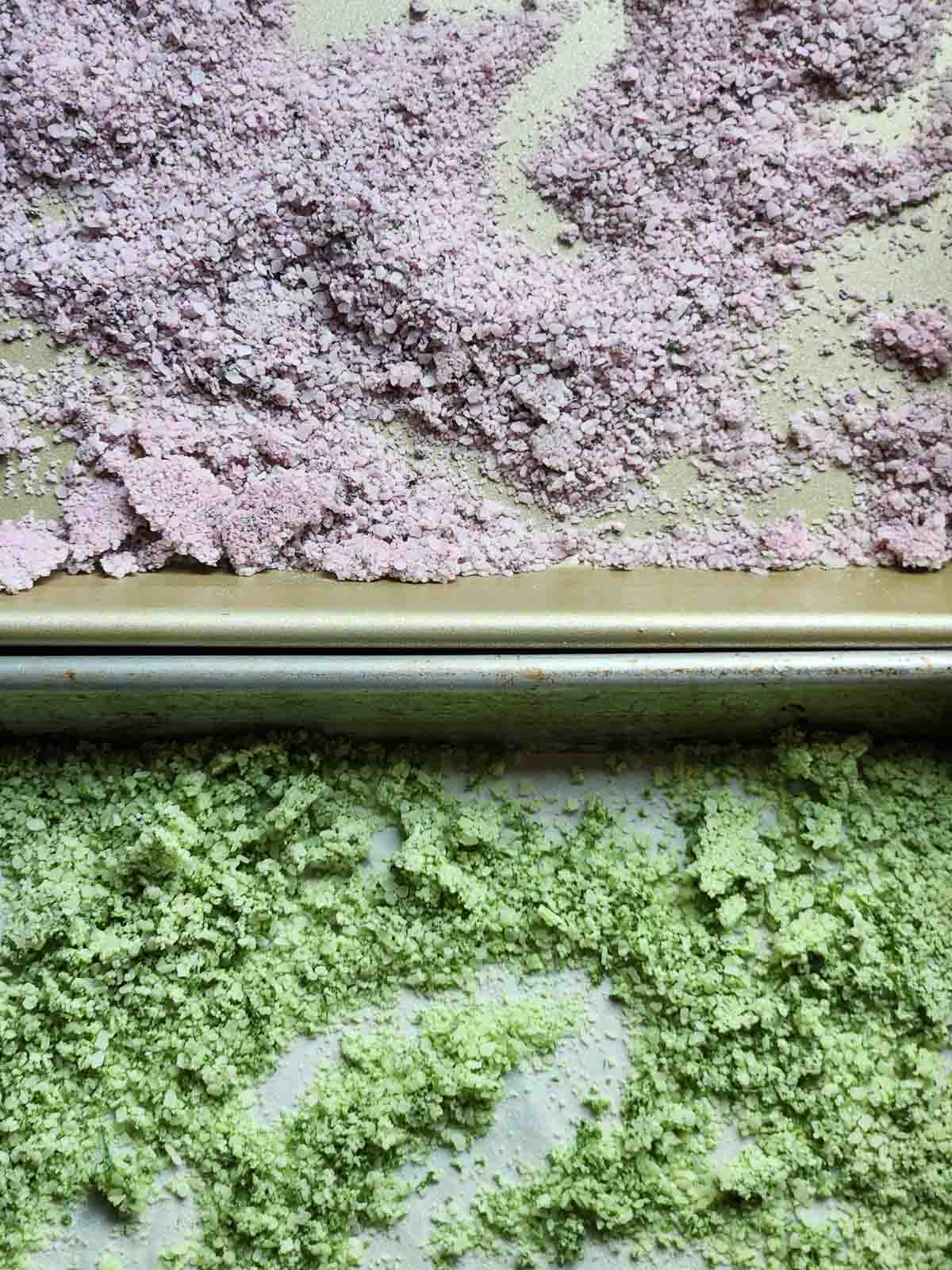 Overhead view of two baking sheets showing dried purple and green basil salt side by side.