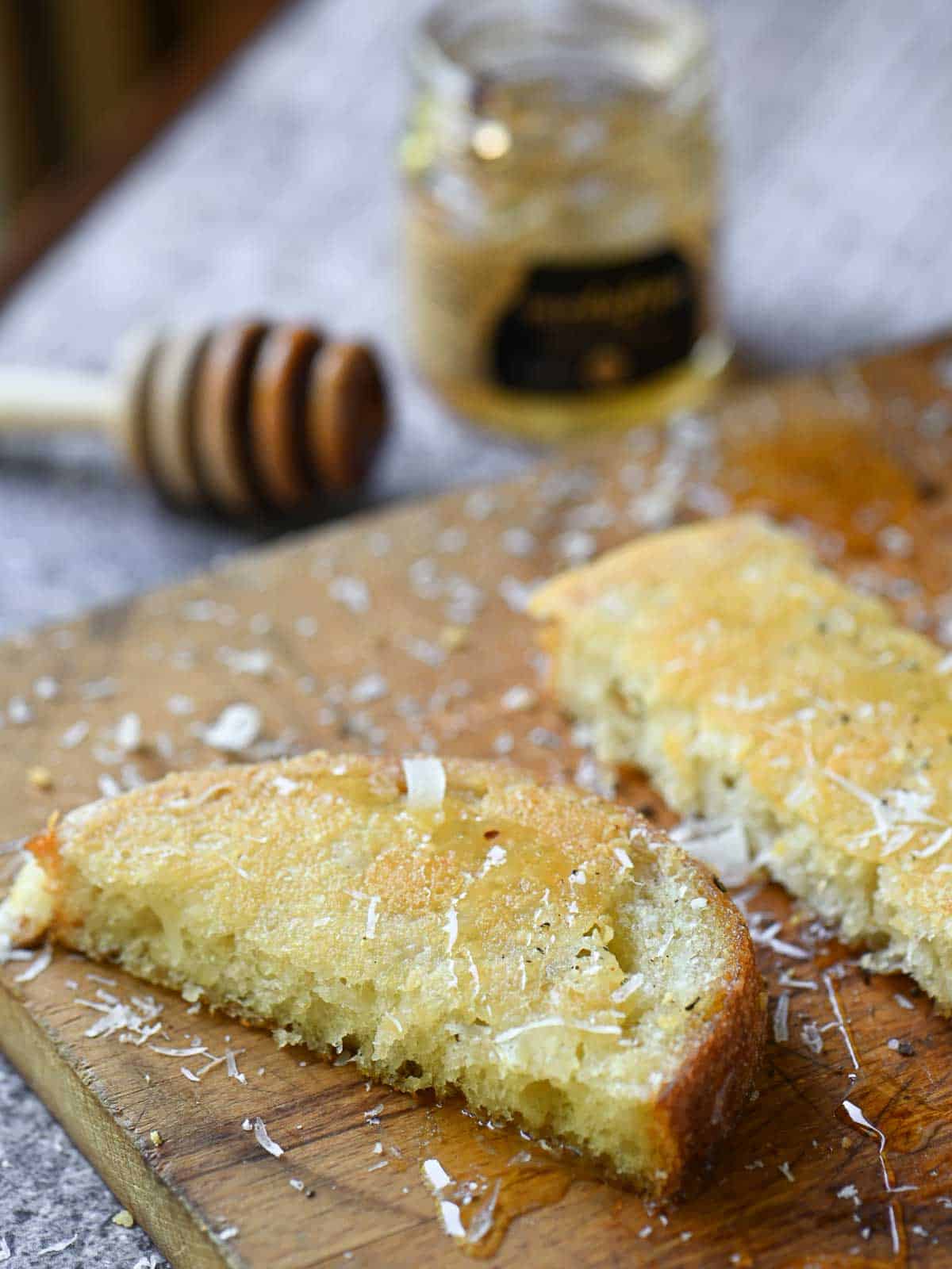 Slices of Parmesan toast on a wooden board with honey in the background.