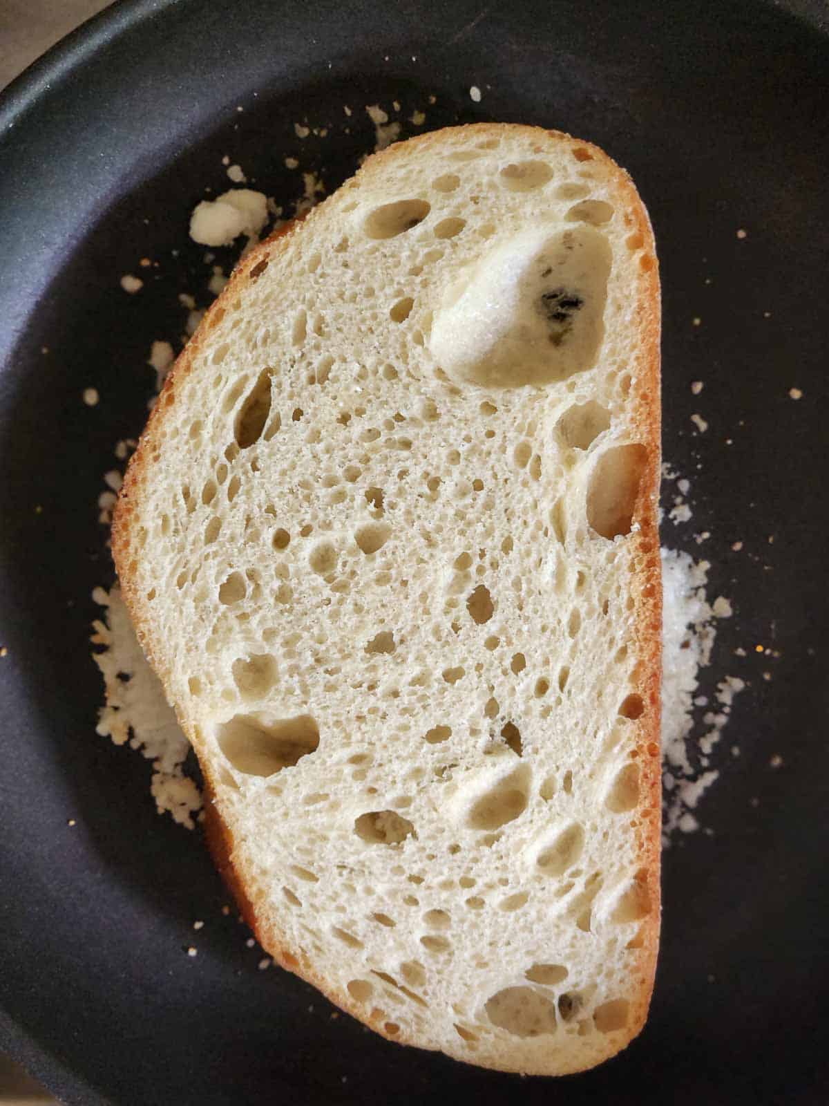 Bread on top of Parmesan cheese in a black skillet.