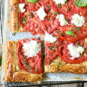 A puffed pastry tomato tart on a metal pan with a slice cut out.