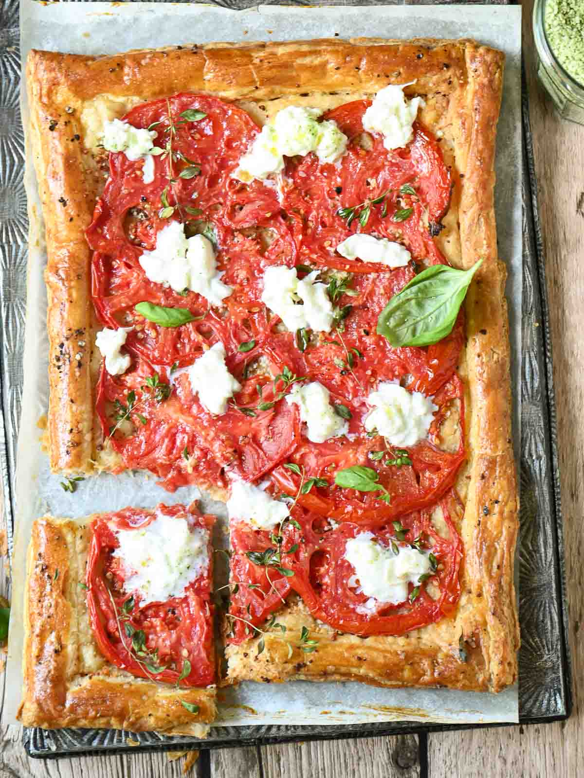 An overhead shot of a tomato tart with stracciatella on top of a metal baking tray.